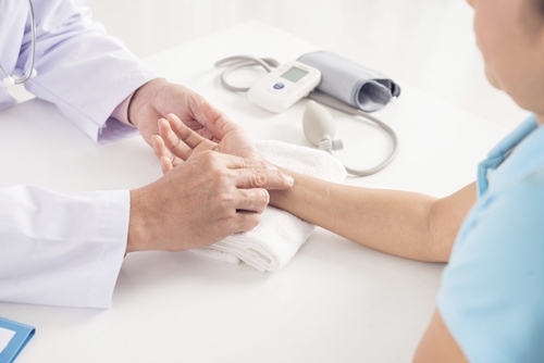 Doctor touching female hand to check pulse